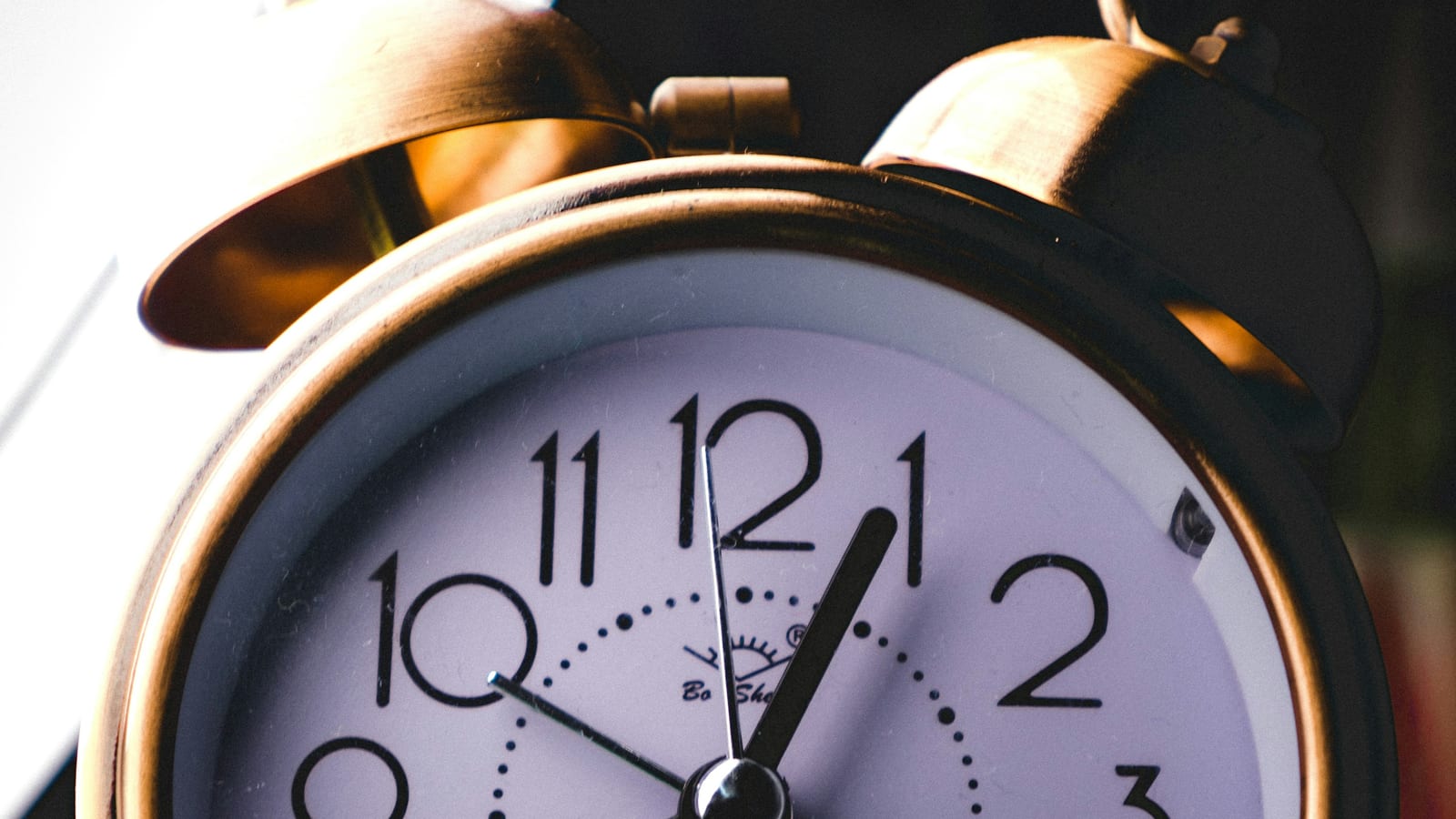 A brass twin-bell alarm clock lit by morning sun coming through a window