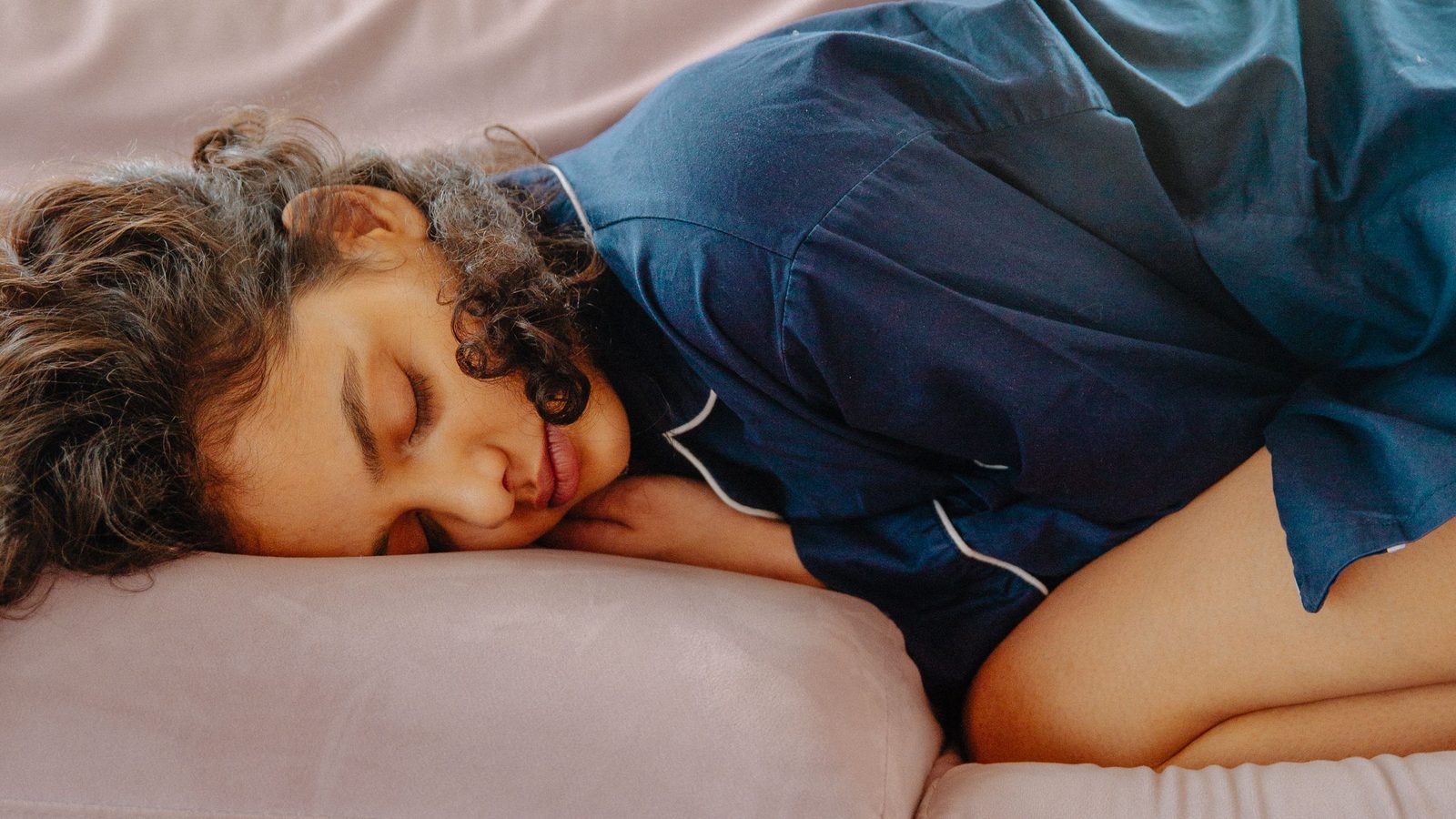 A young woman asleep on a couch in daylight, curled up for an afternoon nap