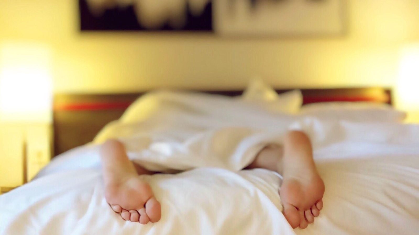 Person's feet on white bedding with warm morning light coming through a window