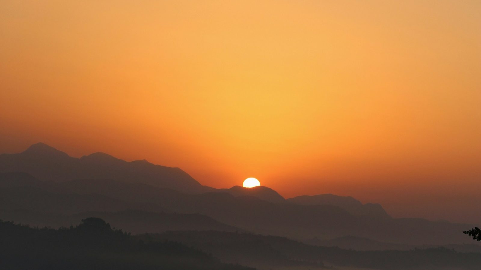 A sunrise over misty mountains with the sun just breaking over the ridgeline, casting warm orange and golden light across the landscape
