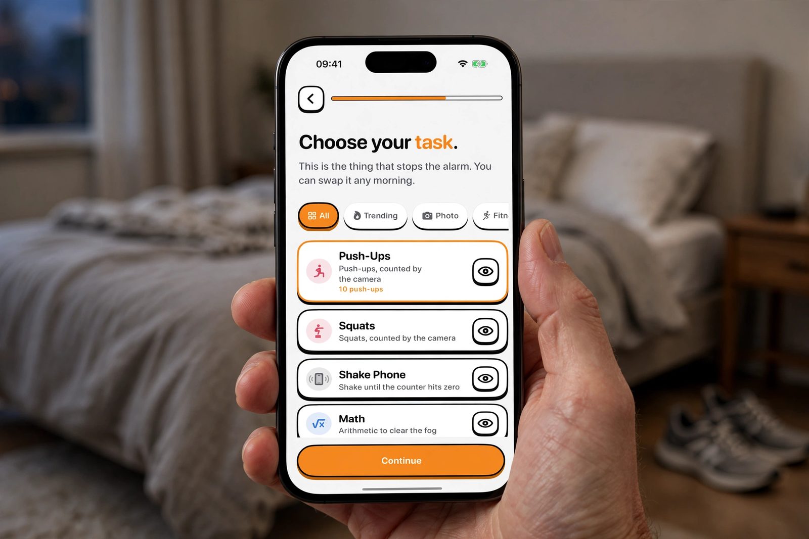 A hand holding an iPhone in a bedroom, showing NoNap's wake task picker with Push Ups, Squats, Shake Phone and Math