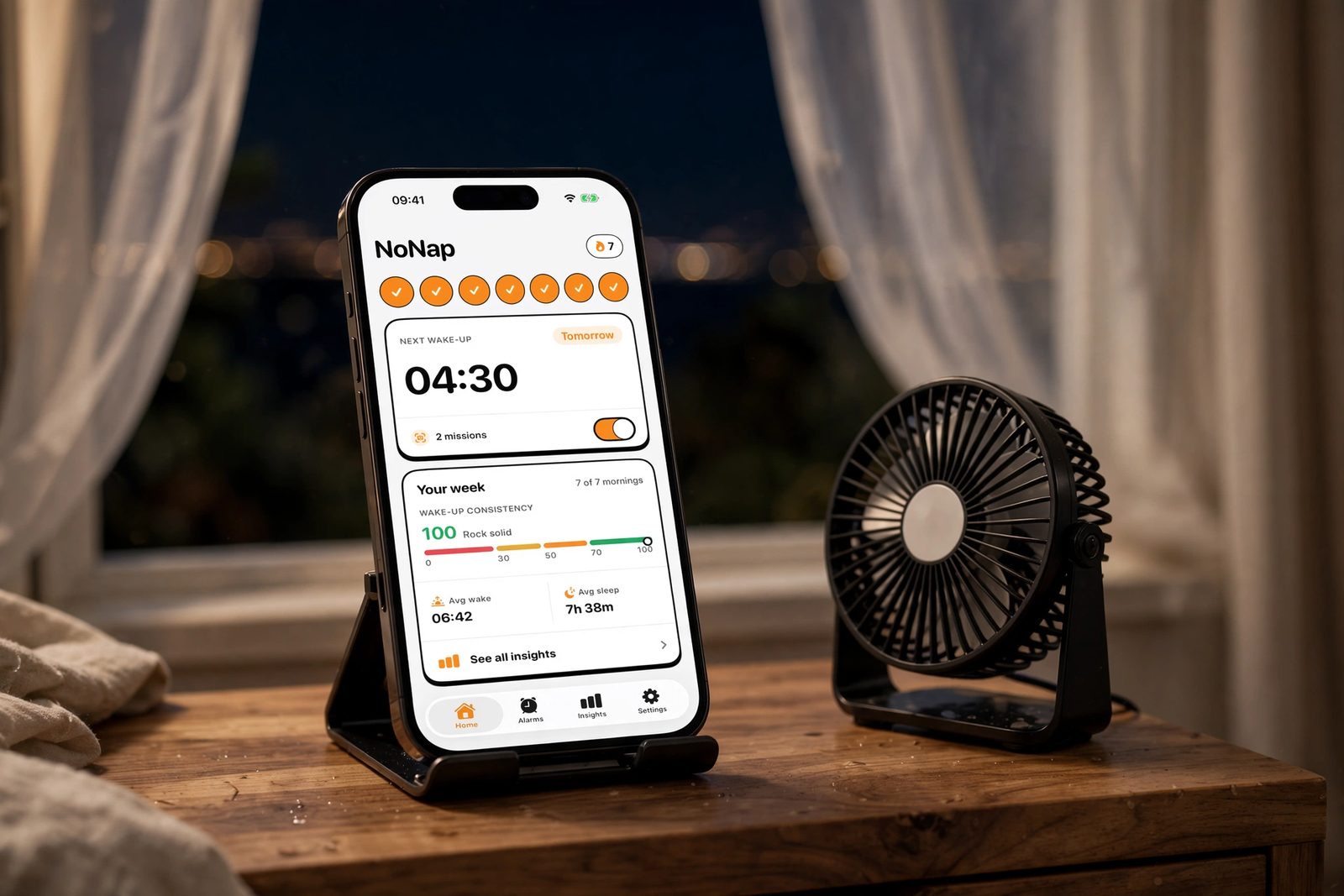 An iPhone on a nightstand next to a small fan by an open window on a summer night, showing NoNap's home screen with a 7 day streak, tomorrow's 4:30 wake-up, and a week of wake-up consistency and average sleep